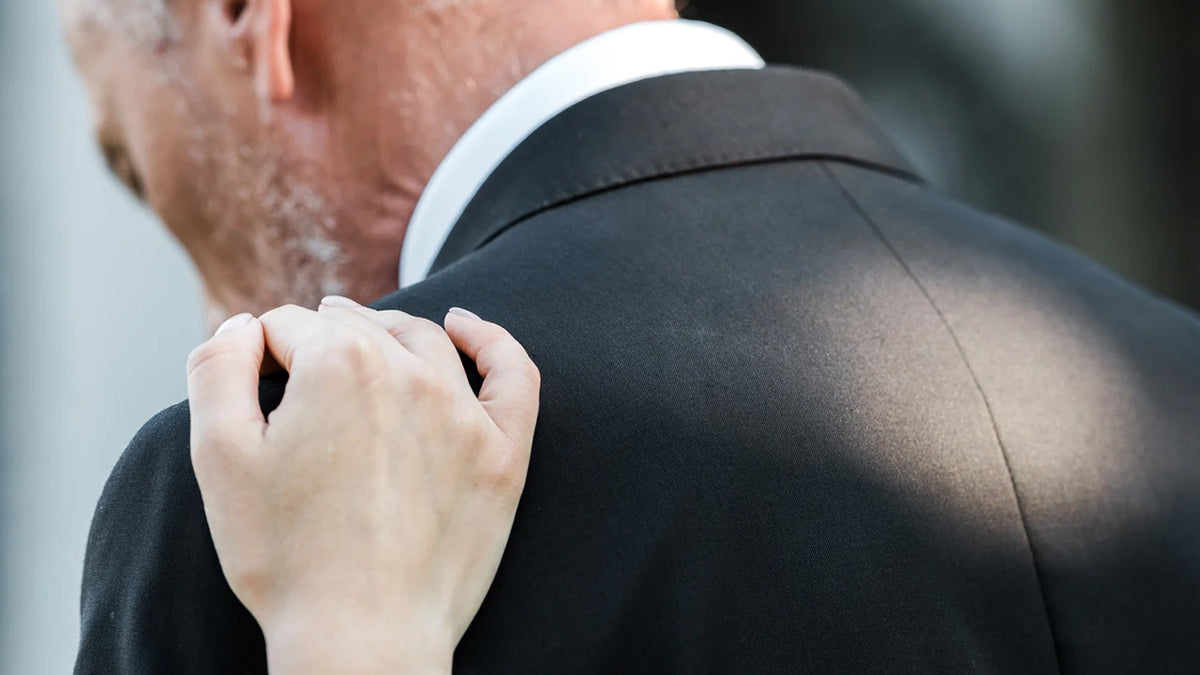 Hand resting on a man's shoulder as a gesture of comfort and support after a death.