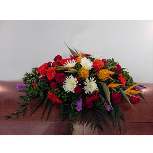 Coussin de cercueil composé de fleurs tropicales et de roses rouges