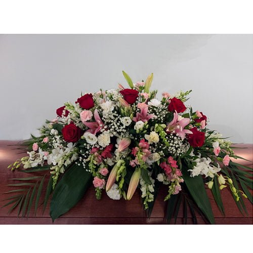 Coussin de cercueil composé de lys, de roses, d’orchidées et mini oeillets